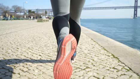 low section of sporty girl running along embankment