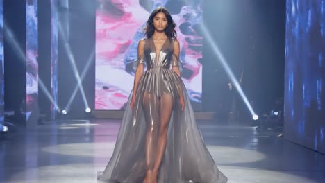 a model showcases a shimmering sheer gown on a runway at a fashion show