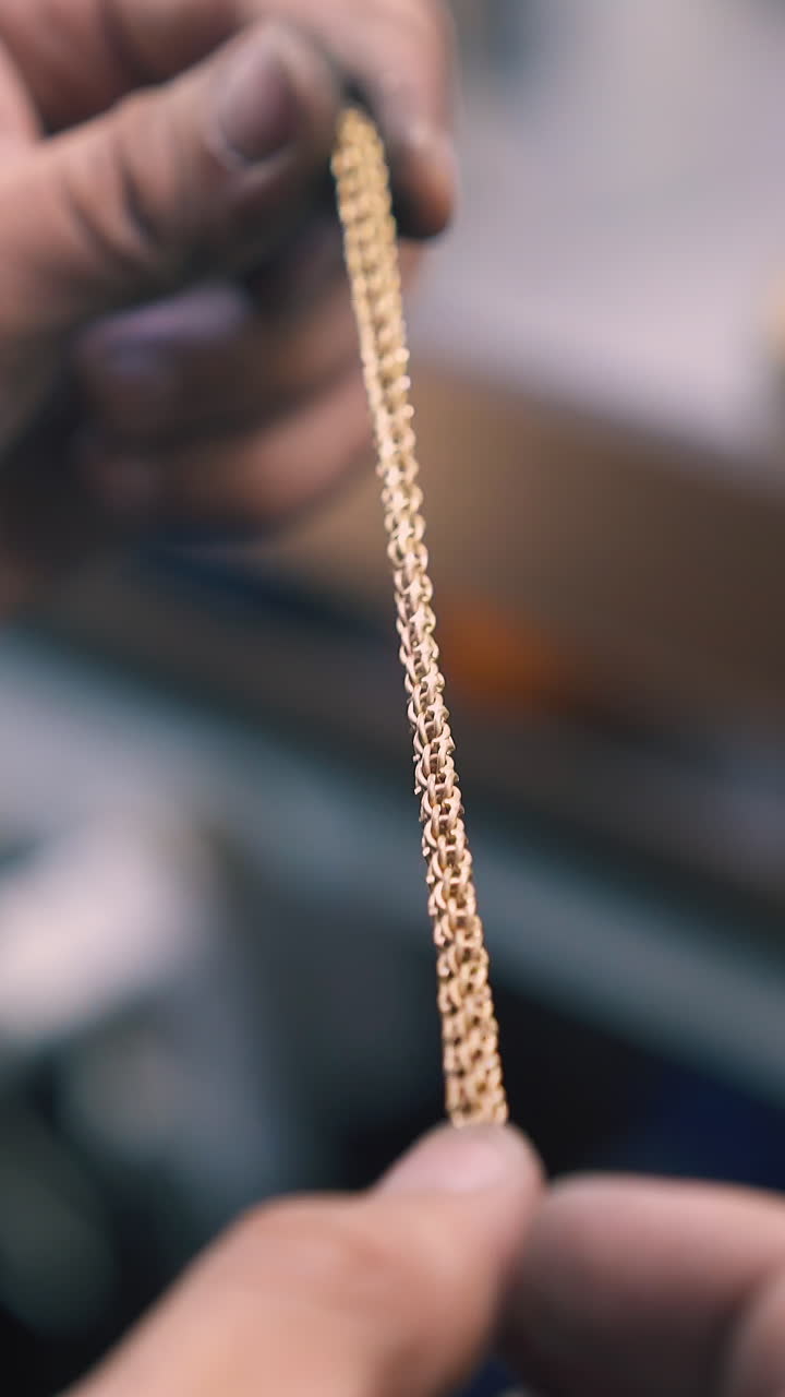 CU: skilled jeweler holds new gold bracelet in hands examining on blurred background in light workshop close view