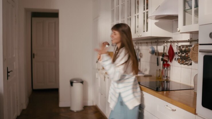 Donna che canta e balla in cucina con un mestolo