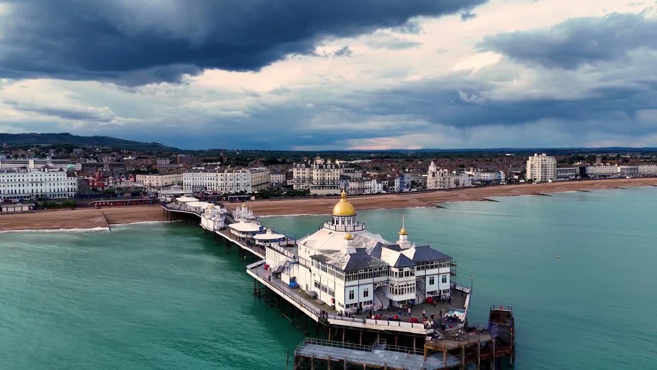 이스트본 피어 (eastbourne pier) 의 숨막히는 공중 풍경을 경험하십시오. 극적인 폭풍우 하늘을 날아다니며 이 상징적인 랜드마크의 놀라운 아름다움과 웅장함을 포착하는 영화적인 플라이오버를 위해.