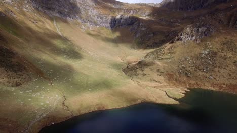 aerial-view-of-mountain-lake-in-Switzerland-during-autumn-with-snowy-mountains,-revealing-shot-with-massive-mountain-front