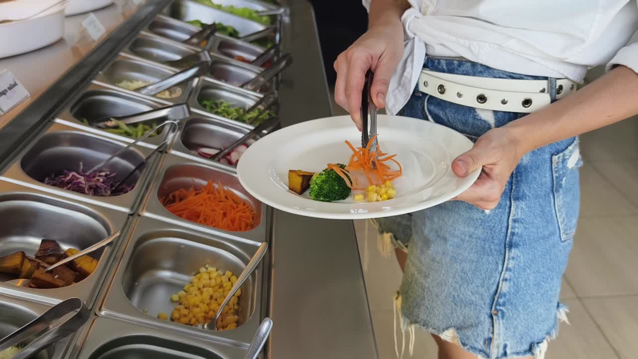 mujer en una barra de ensaladas seleccionando verduras