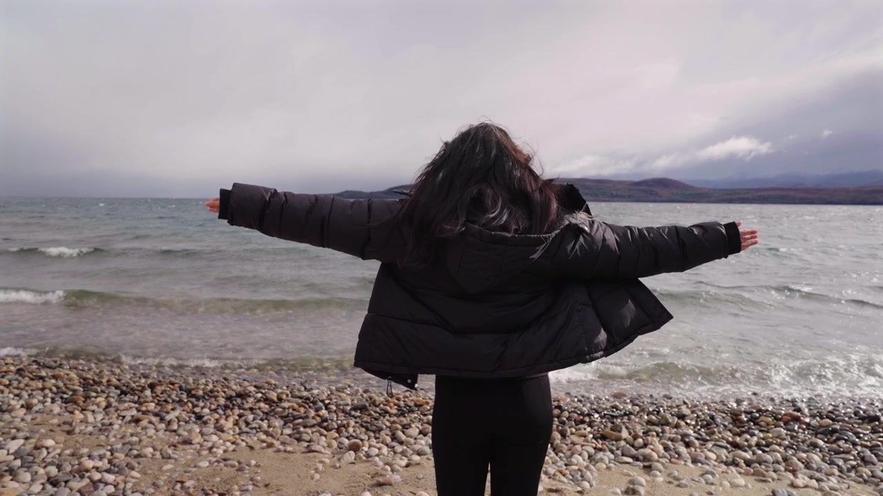 Patagonia Argentina. Silueta de mujer de pie en la orilla del lago Nahuel Huapi con los brazos abiertos. Conexión con la naturaleza.