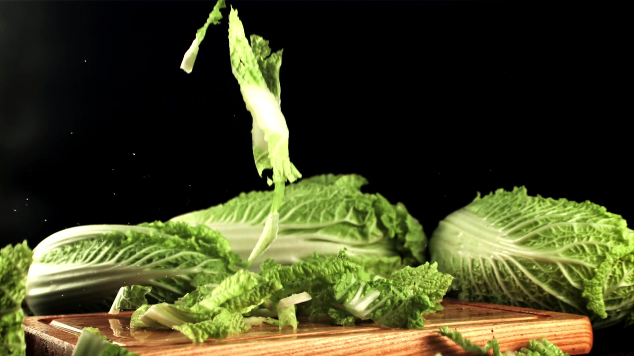 Chopped Chinese Cabbage Leaves Falling onto a Wooden Cutting Board in Slow Motion