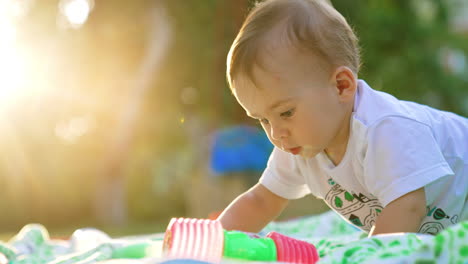 adorable one-year-old boy playing outdoors in the rays of sun. lovely kid waving with a toy hammer. side view. close up. blurred backdrop.