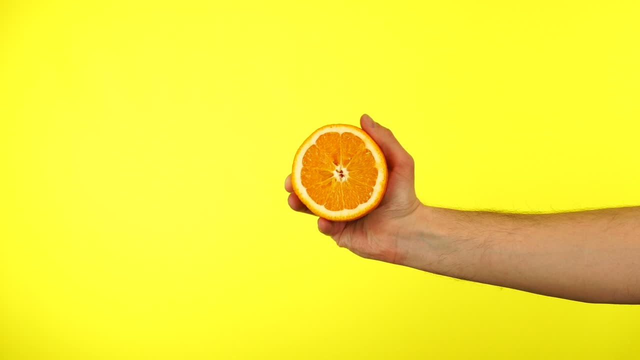 hombre con una mano sosteniendo una naranja fresca sobre un fondo amarillo