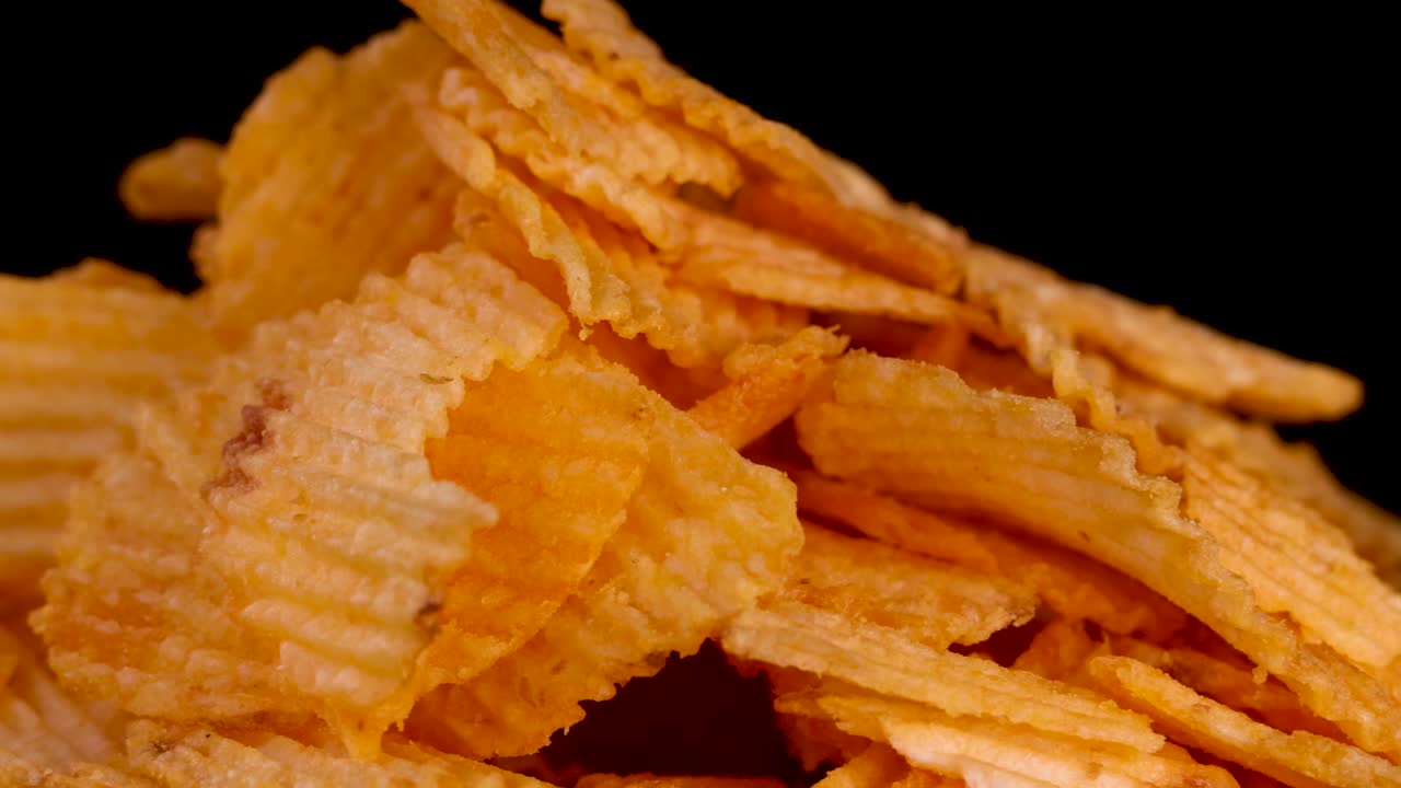 Golden ridged potato chips rotate smoothly under studio lighting, crisp texture highlighted by black background