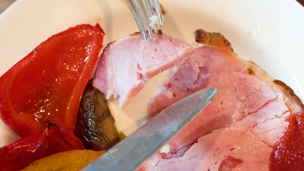 Person Cutting and Eating Sliced Ham with Roasted Vegetables