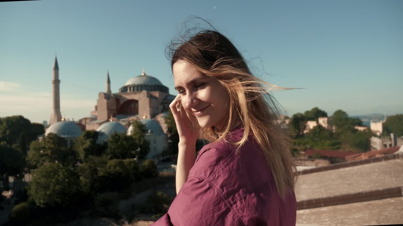 Jeune et belle femme touriste heureuse posant, les cheveux au vent, devant la magnifique Sainte-Sophie sous le soleil estival, en Turquie