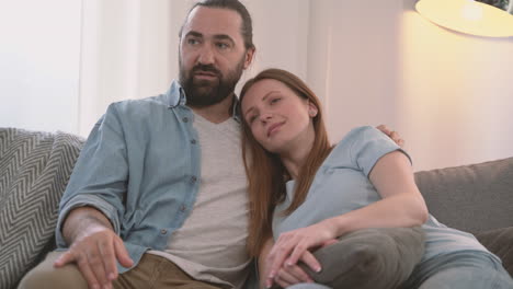 bearded man converses with his partner, an attractive woman, who rests her head on his shoulder