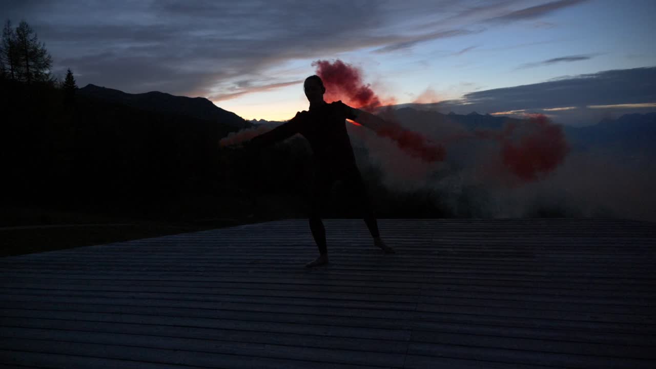cámara lenta: hermosa foto de la silueta de una mujer joven bailando en una plataforma al atardecer sosteniendo una bengala de humo púrpura