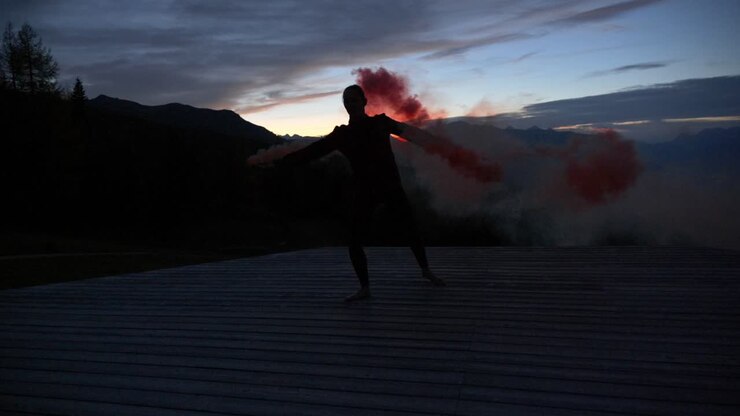Rallentatore: Splendida ripresa della silhouette di una giovane donna che balla su una piattaforma al tramonto, tenendo un fumogeno bengala viola.