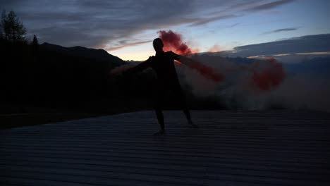 Slow-motion:-Beautiful-shot-of-silhouette-of-a-young-woman-dancing-on-a-plattform-at-dusk-holding-purple-smoke-bengala-flare