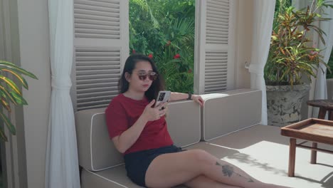 Woman-relaxing-under-the-shade-while-using-her-cellphone-in-a-tropical-island-during-a-sunny-morning