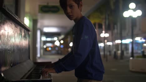 young boy plays piano in street