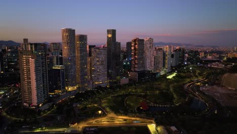 Descending-drone-shot-of-skyscrapers-in-Santa-Fe,-colorful-sundown-in-Mexico