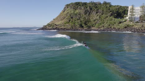 Surfers-Enjoying-The-Waves-At-The-Beach,-Burleigh-Head-National-Park-In-Queensland,-Australia---aerial-drone-shot