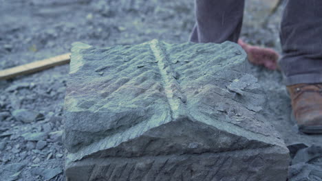 Handheld-shot-showing-a-stone-craftsman-creating-a-sloped-edge-on-top-of-a-stone-pillar,-shot-outside-in-the-city-of-Ancud,-Chiloe-Island