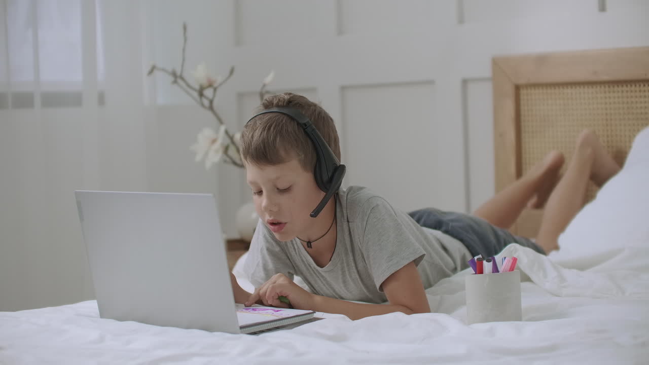 niño en edad preescolar está aprendiendo a dibujar en casa escuchando música y entrenando video a través de auriculares por computadora portátil