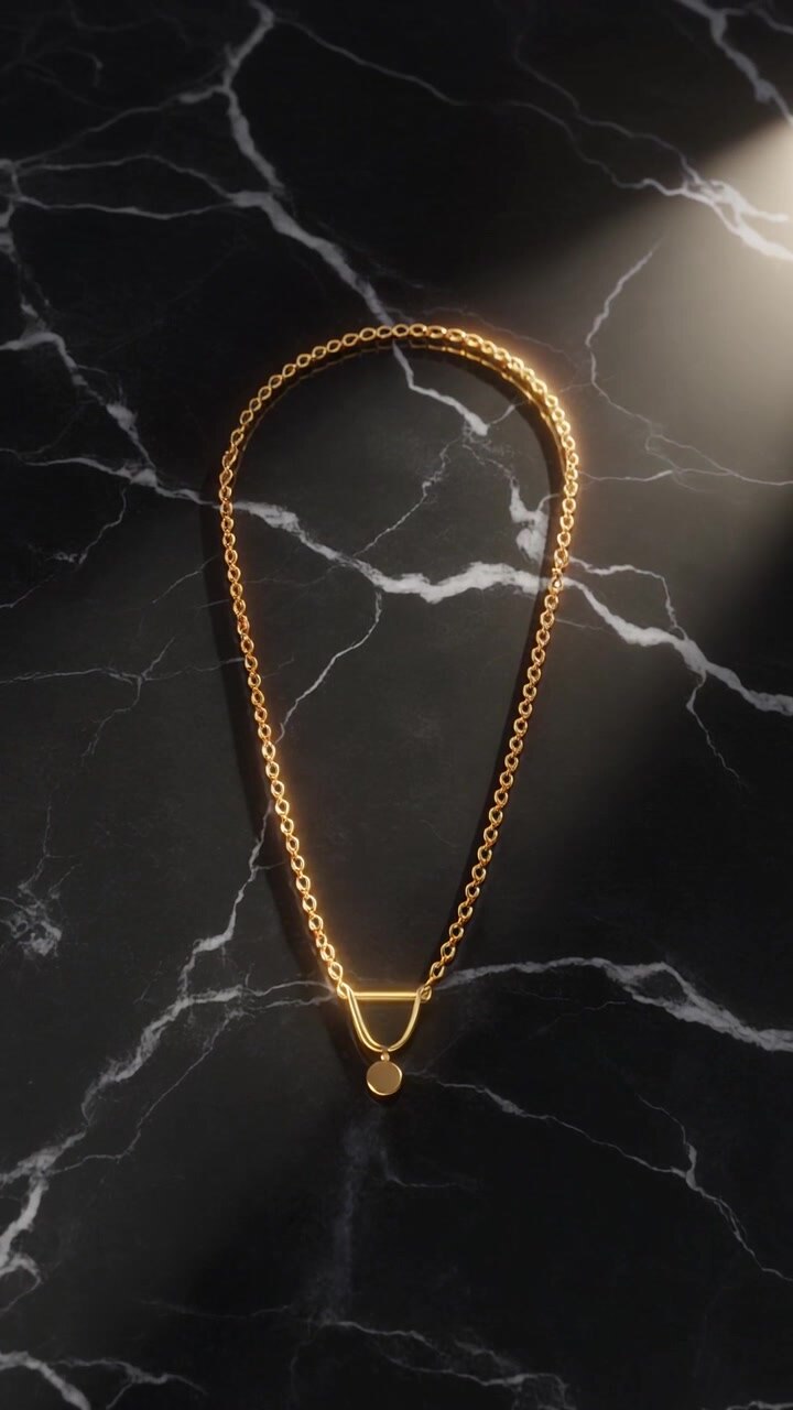 Una collana con ciondolo geometrico dorato poggia su uno sfondo di marmo nero sotto un raggio di luce soffusa