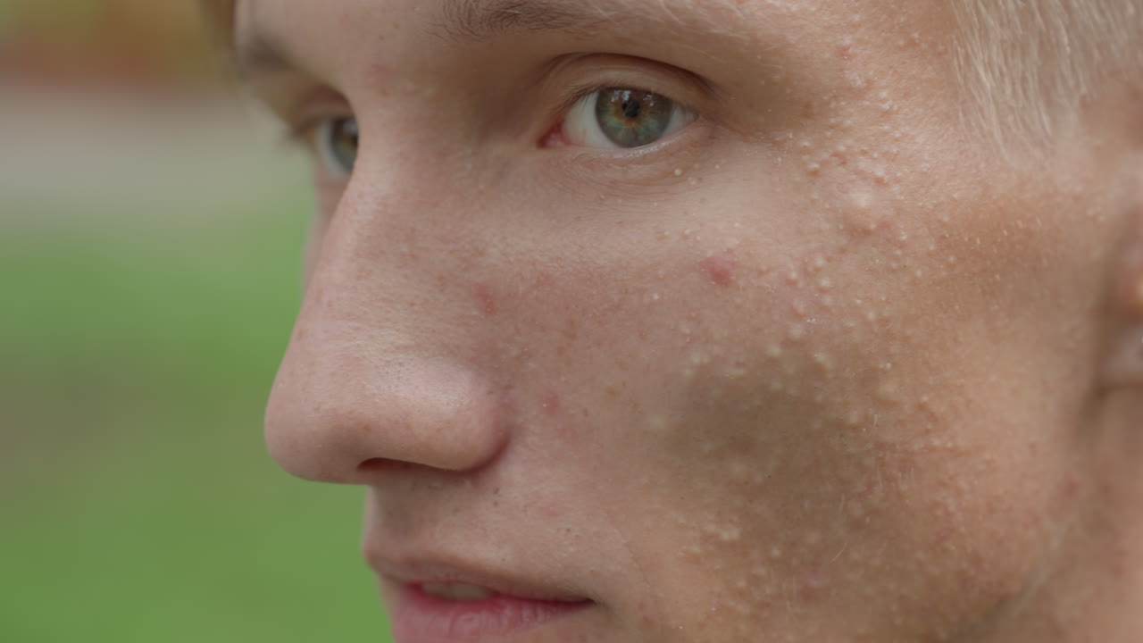 Profil-Nahaufnahme eines kaukasischen Mannes, der im Freien lächelt, modellhafte Seitenansicht mit subtilem Grinsen, Schauspieler, der auf ein ungesehenes Stichwort reagiert, Student, der mit einem Freund einen Witz teilt, Passant, der mitten im Gehen innehält, sichtbare Hautstruktur