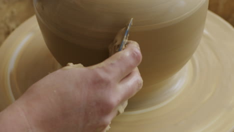 Handheld-shot-of-rolling-a-scraper-tool-scraping-the-side-of-a-big-brown-vase,-female-doing-pottery-in-her-studio