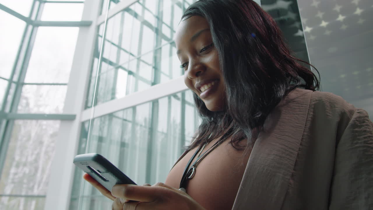 Positive Black Businesswoman Using Smartphone in Elevator