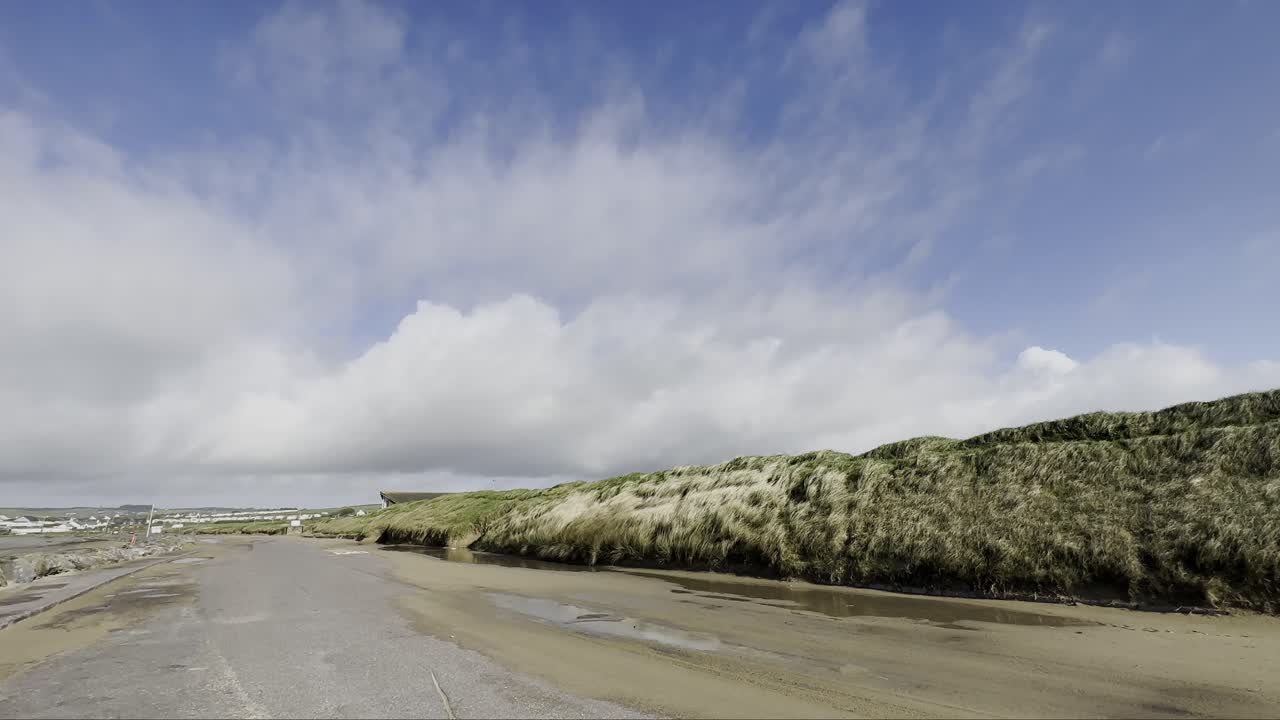 carretera costera ventosa cubierta de arena y nubes moviéndose rápido