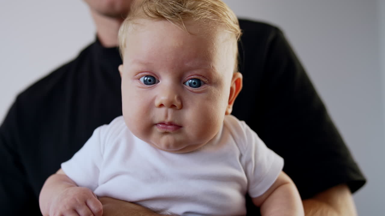 Unrecognized man in black t-shirt holding his baby. Little cute lid looking at camera with surprise. Close up.