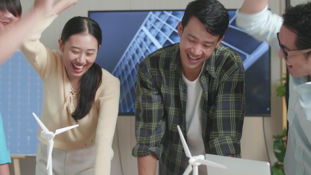 아시아 엔지니어 그룹이 사무실에서 태양 전지판을 가진 작은 집 모델을 작업하는 동안 함께 손을 고 있습니다.