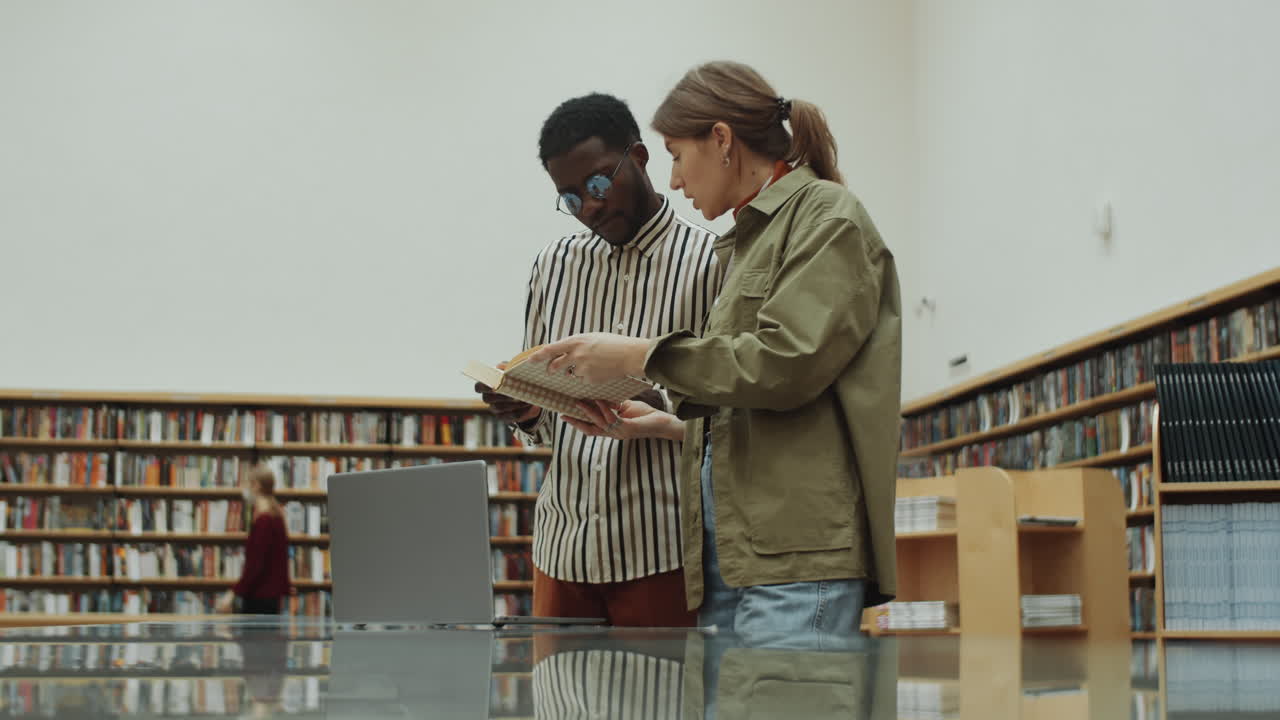 hombre y mujer multiétnicos leyendo libros y usando computadora portátil en la biblioteca