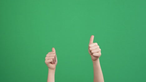 아이가 누군가를 가리키고, 일어서서, 초록색 스크린 배경에 두 손 엄지손가락을 보여주고 있습니다.