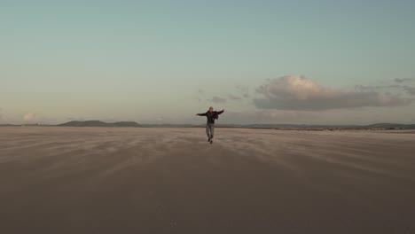 Man-walking-on-sandy-beach-at-sundown