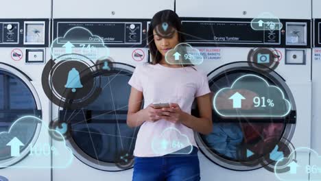 cloud upload icons floating against african american woman woman using smartphone at laundromat shop