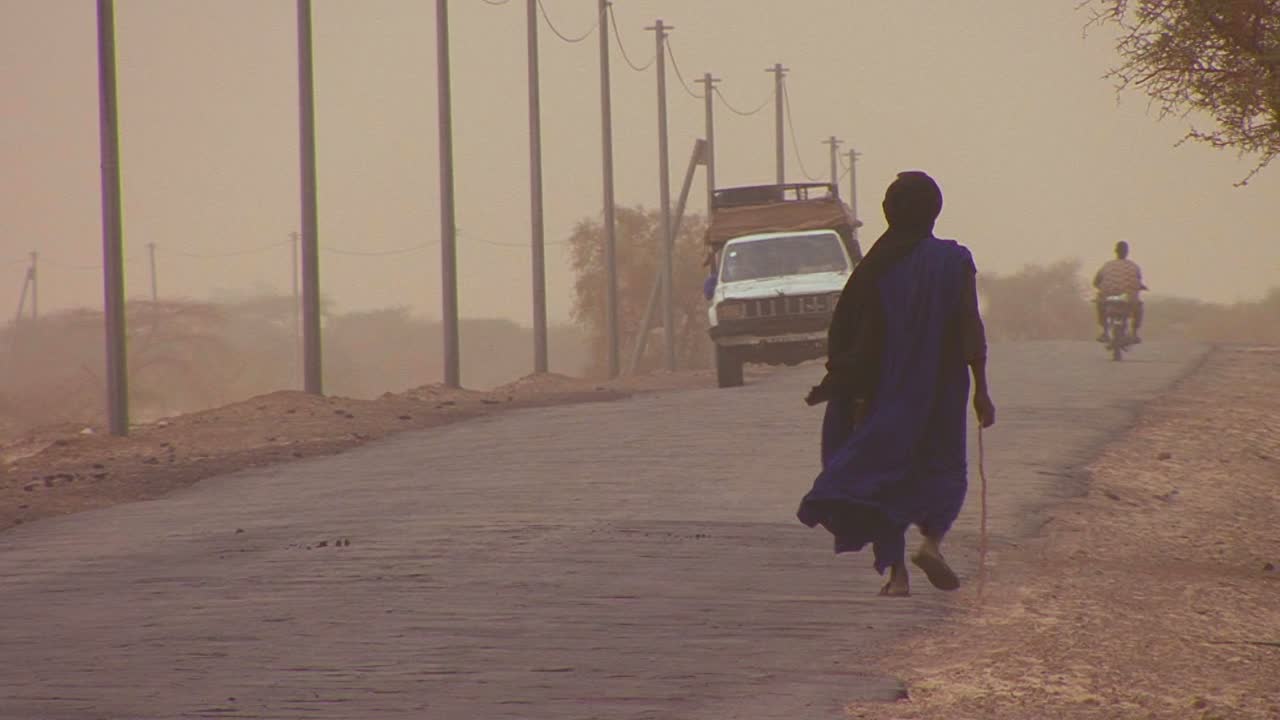 una persona touareg camina por un camino a través del desierto del sahara en mali durante una tormenta de viento