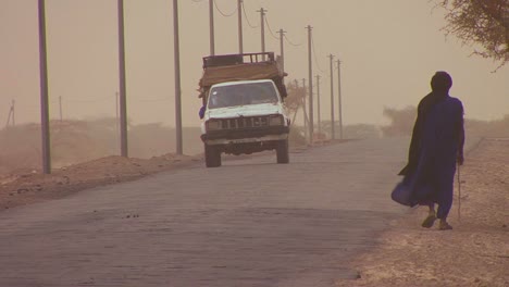 a touareg person walks down a road through the sahara desert in mali during a windstorm