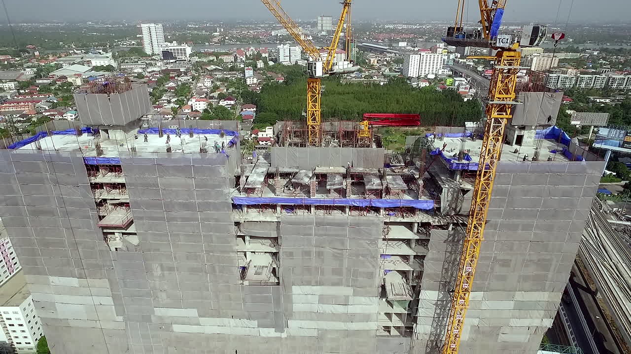 Aerial view of a building construction site with workers assembling the structural framework, machinery in operation, and materials arranged across the work area in an active urban project