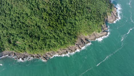 Aerial-view-of-a-jagged-rock-island,-surrounded-with-lush-green-nature-and-Hong-Kong-bay-water