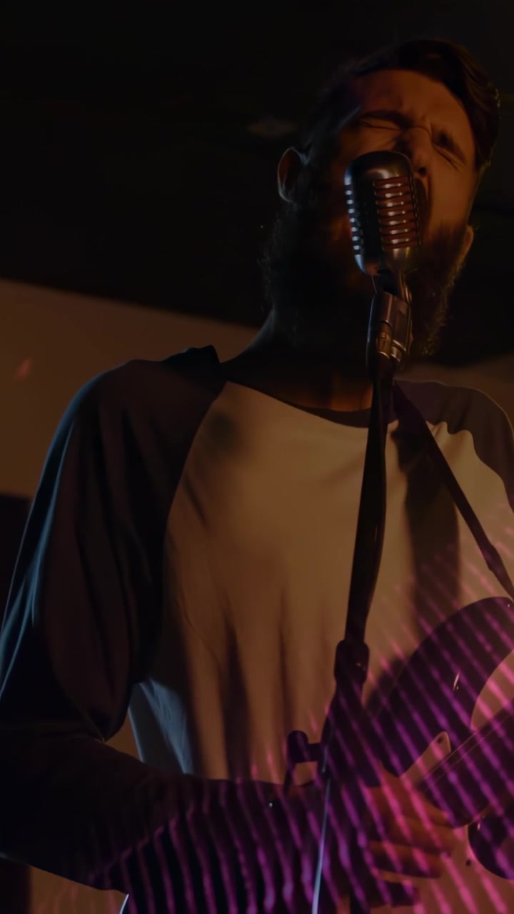 Video verticale: Telecamera che si avvicina, cantante solista con chitarra che si avvicina al microfono, canta, band che si esibisce.
