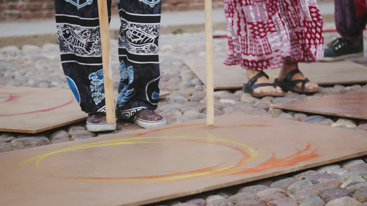 Unge gadekunstnere, der trommer på en træplade på jorden i farverigt tøj under en sommerfestival