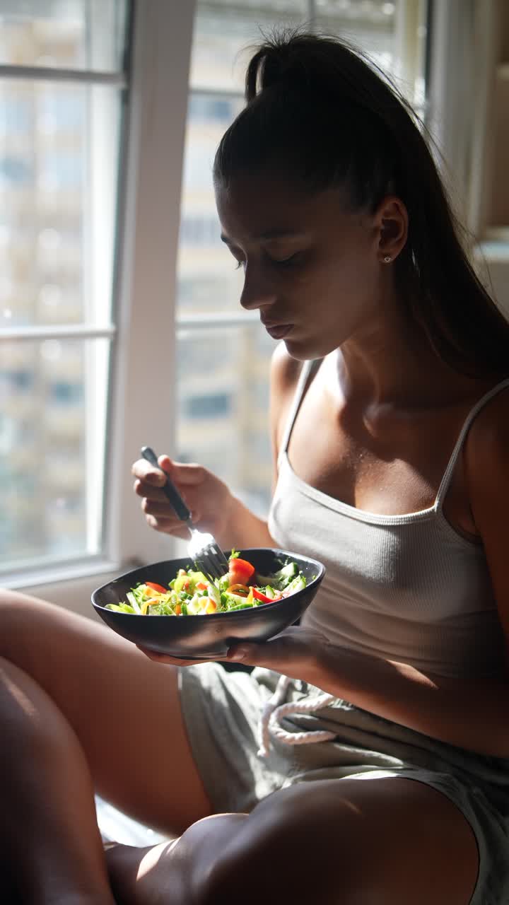 mujer comiendo ensalada en una ventana