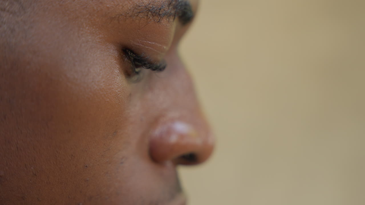 Closeup black man profile tearful and exhausted, sweat and tear tracing cheek, eyes lowered and breathing heavy, shallow depth of field with warm tones, intimate cinematic portrait of release