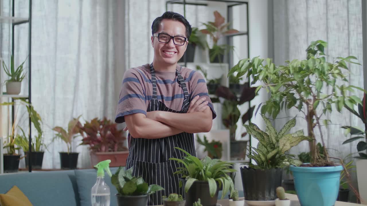 Pria Asia dengan tanaman melipat tangan dan tersenyum ke kamera di rumah