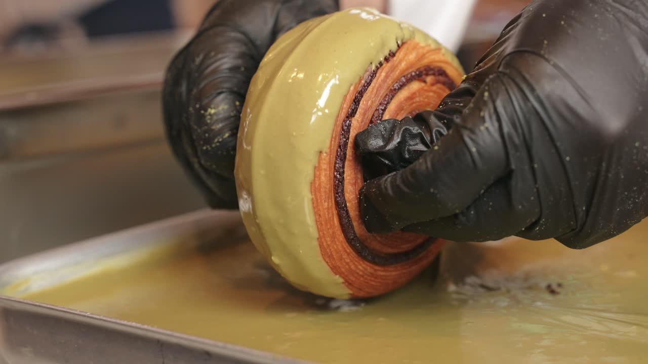 donut de croissant de pistacho siendo decorado rodando sobre el lado que gotea de crema
