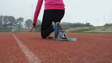 vista trasera de una atleta tomando la posición de salida en la pista de carrera 4k