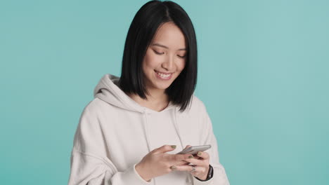 Asian-woman-texting-on-smartphone-and-smiling-at-the-camera.