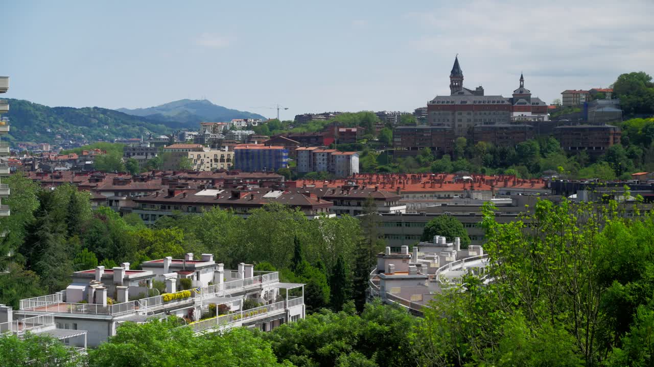 Scenic soft pan over traditional red tile rooftops and modern apartments nestled in green hills in San Sebastian