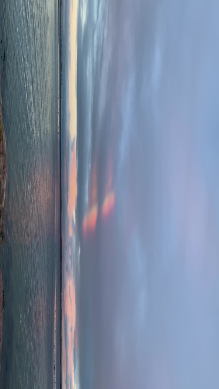 Vertical video of ocean with a fleeting rainbow in the clouds, creating a serene effect