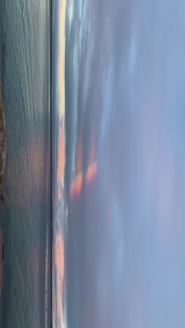 vertical video of ocean with a fleeting rainbow in the clouds, creating a serene effect